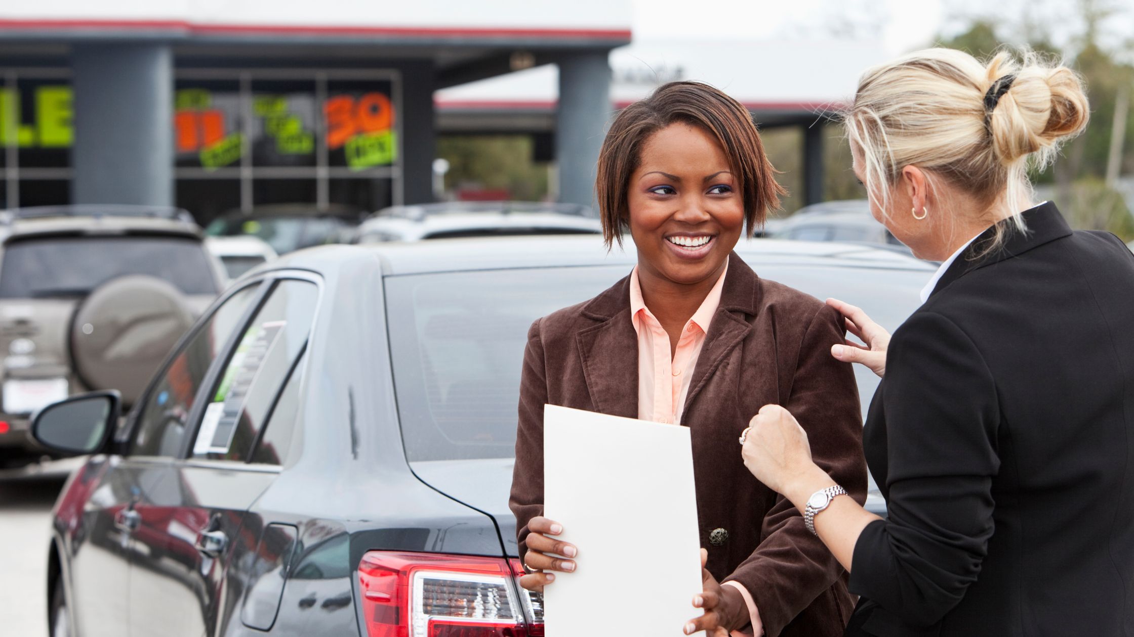 woman in suit with papers in hand at car dealership